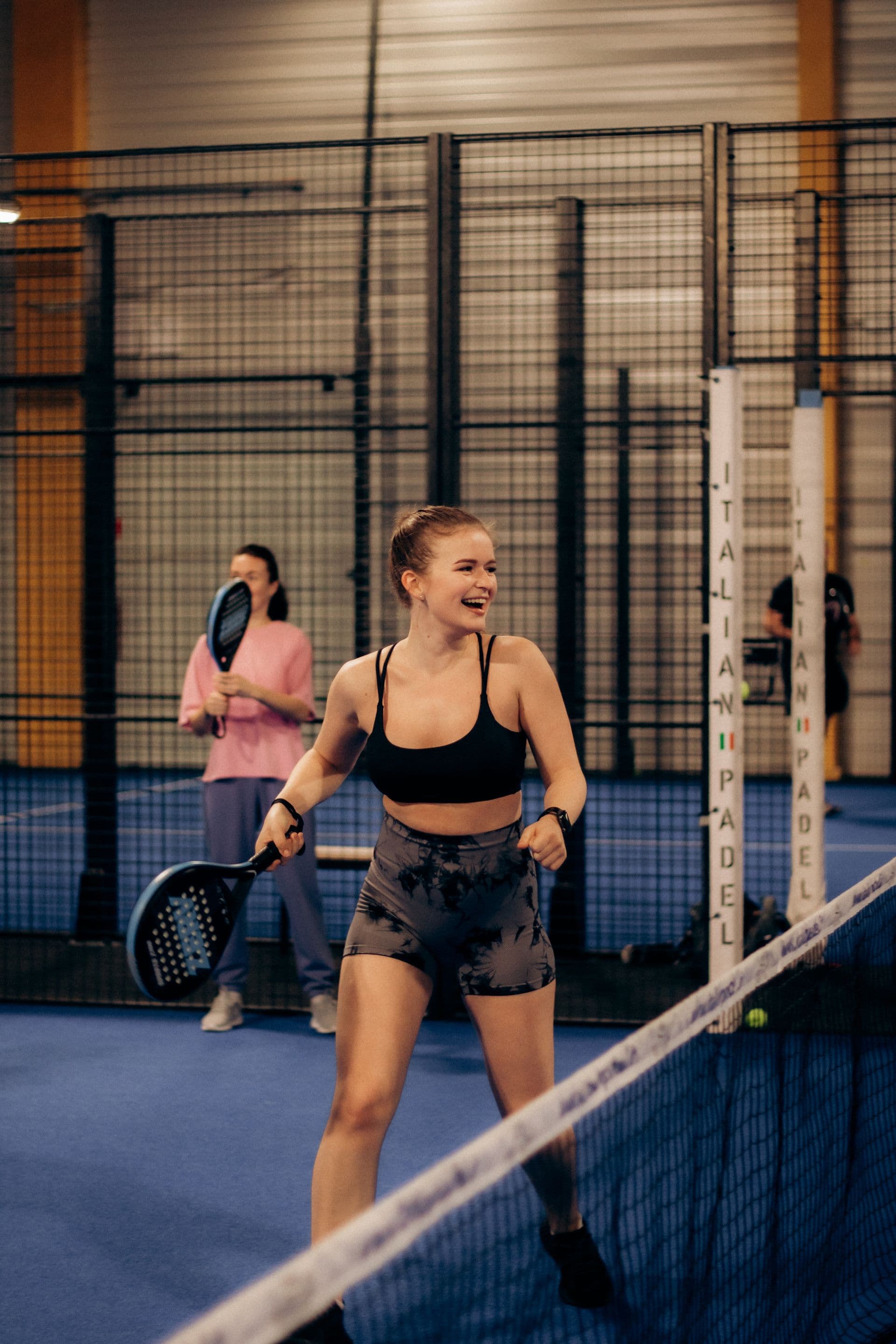Player laughing mid-game on an indoor padel court — illustrative photography, not a Courvia event