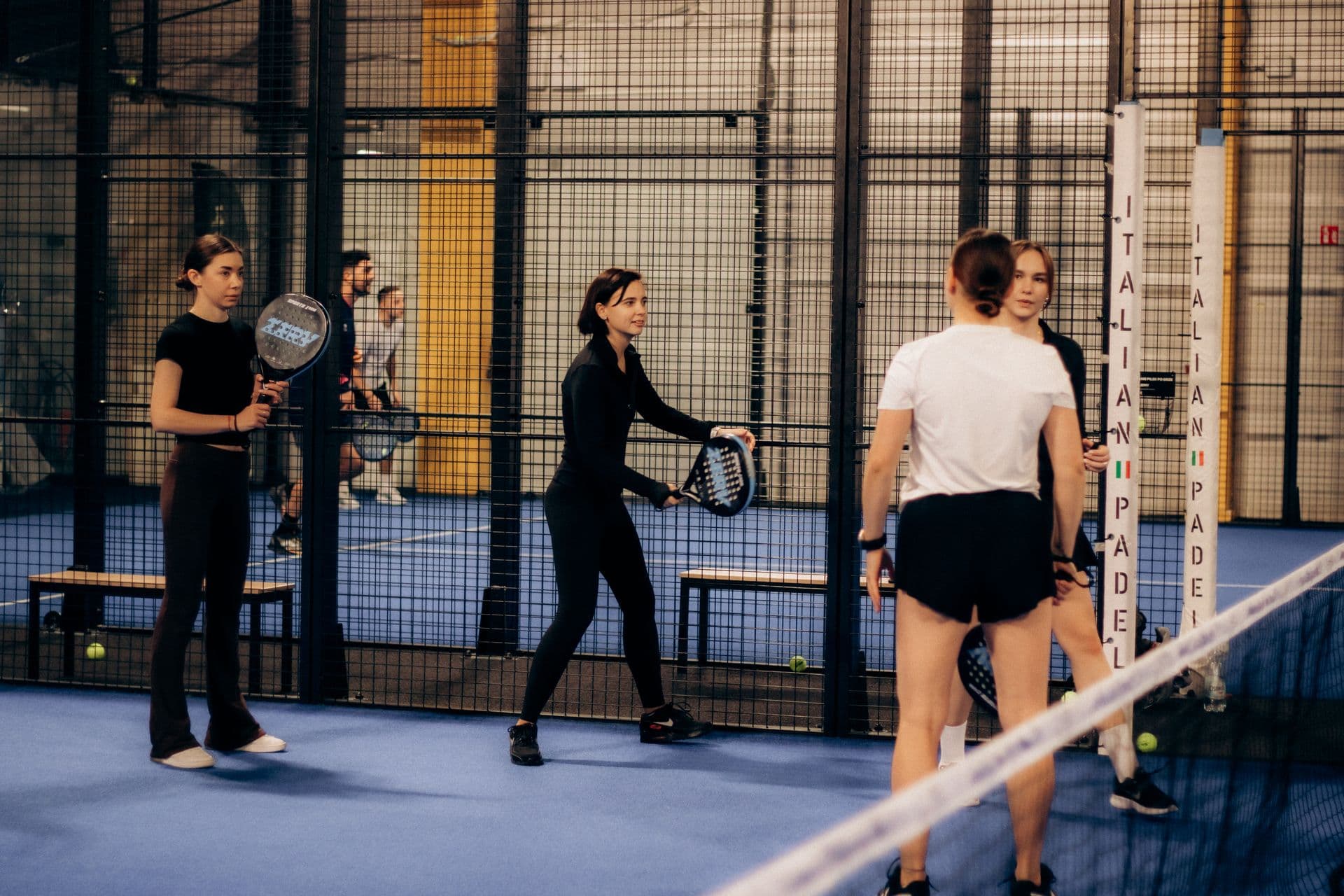 Group of colleagues playing padel doubles together on an indoor court — illustrative photography, not a Courvia event