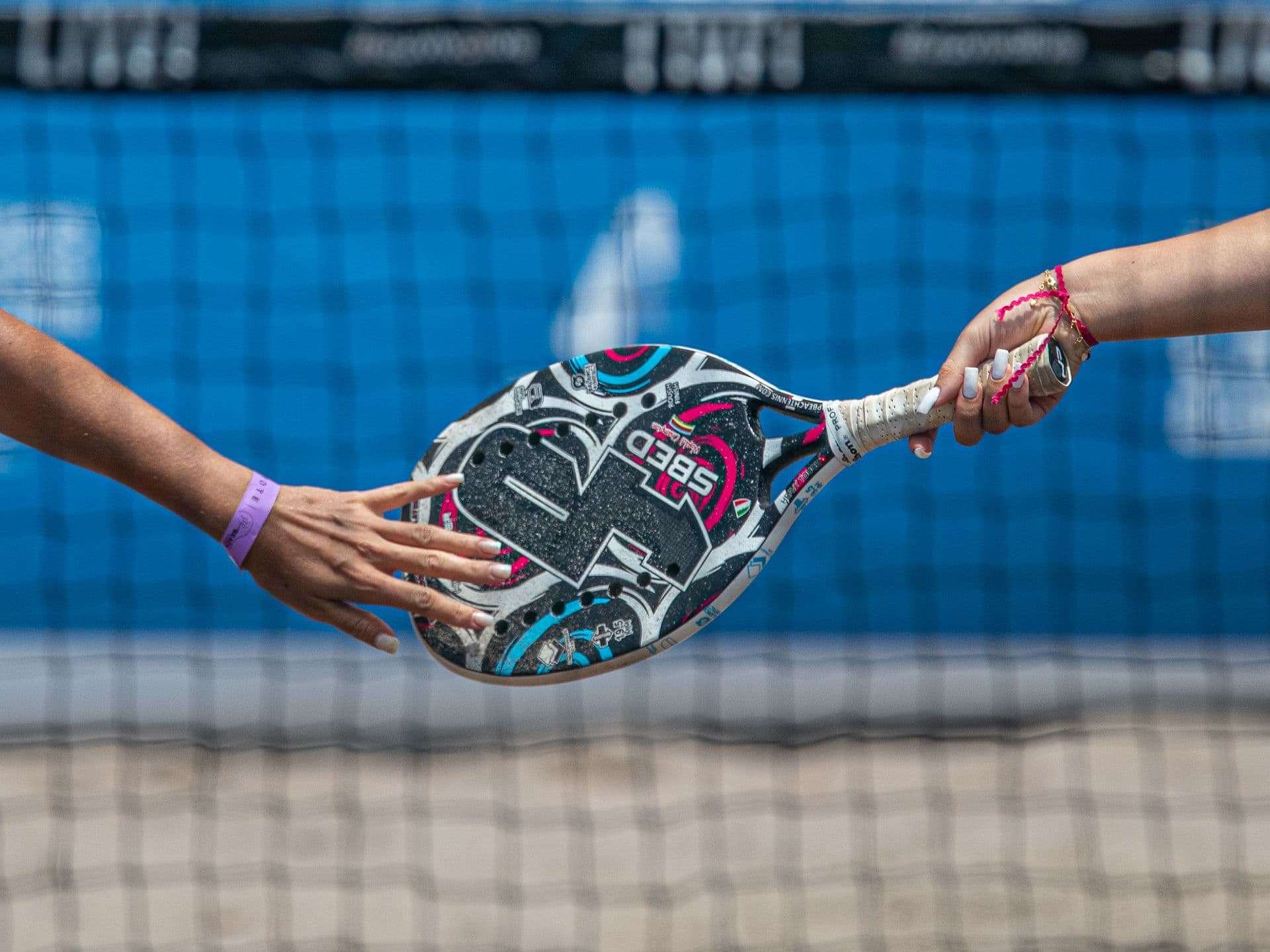 Two players exchanging a padel racket over the net — illustrative photography